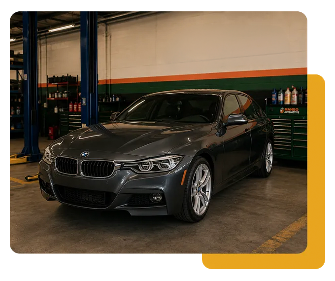 Dark gray BMW parked in an auto shop garage with a lift and tool cabinets nearby