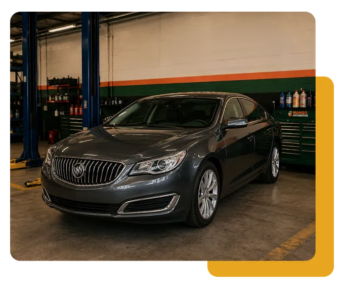 Dark gray luxury sedan in a garage with blue lift and tool cabinets, front view.