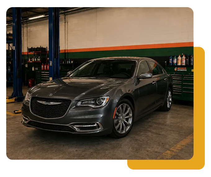 Dark gray luxury sedan in an auto shop garage, parked beside blue lifts and tool cabinets.
