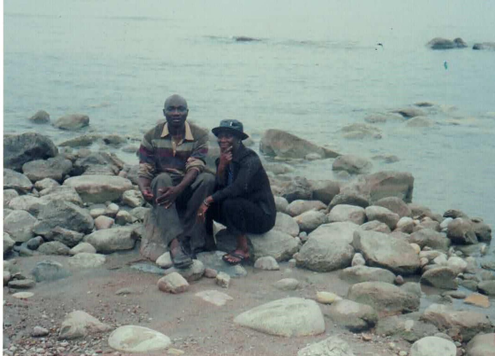 Two people seated on rocks near a body of water on a cloudy day.