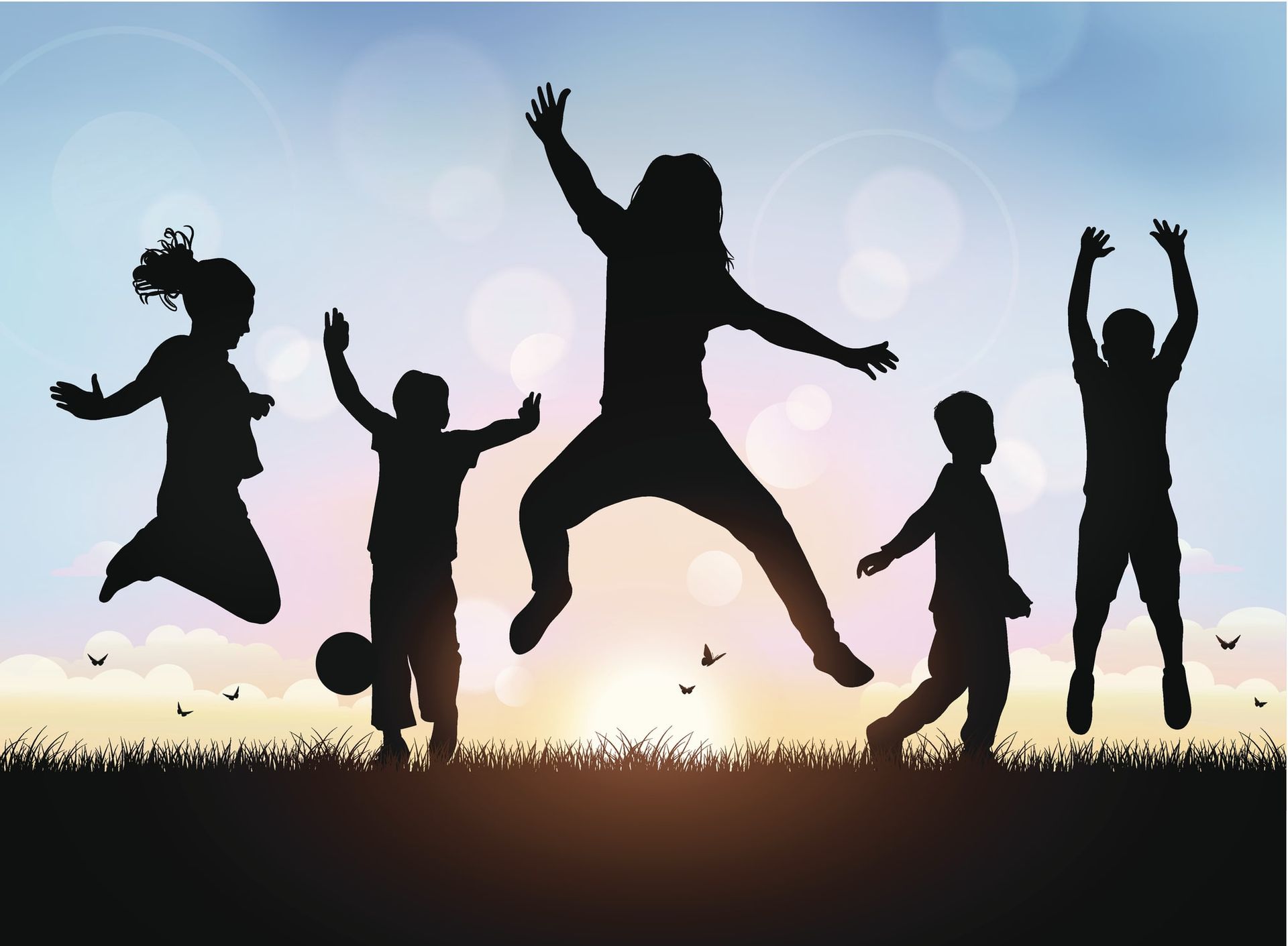 Silhouettes of five children jumping joyfully in a grassy field against a sunset.