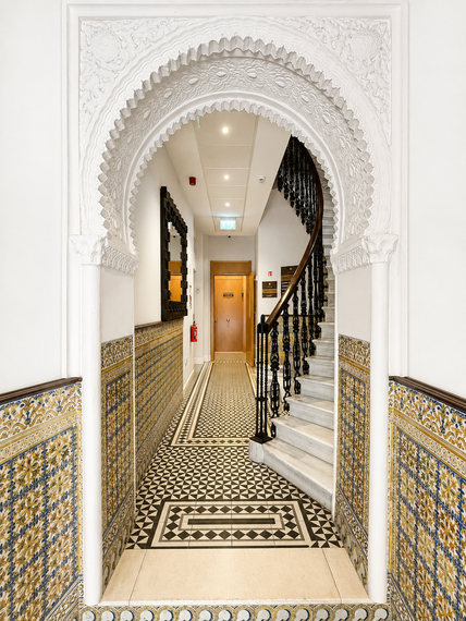Ornate tiled hallway with arched doorway and staircase leading up to a wooden door