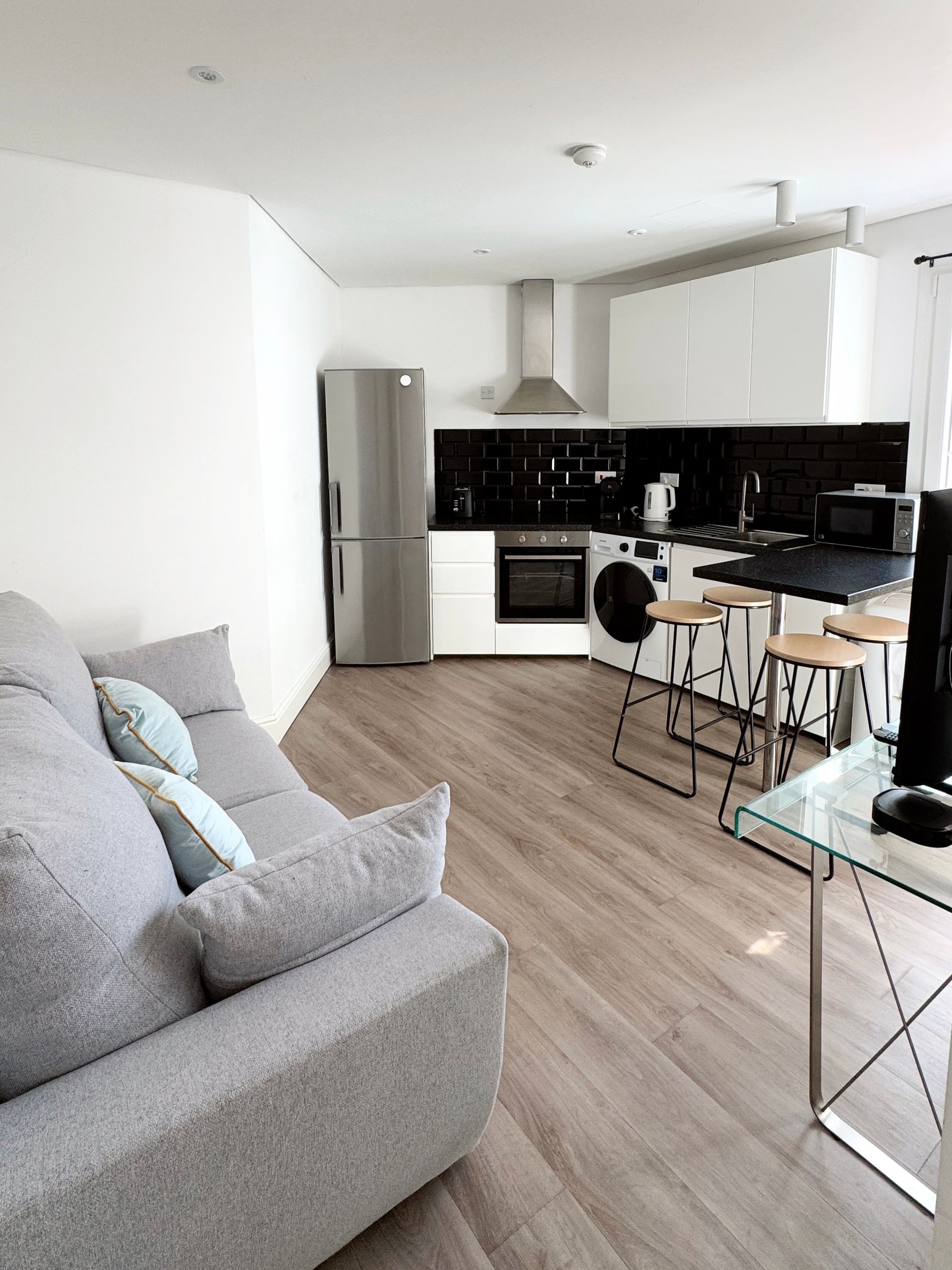 Bright modern apartment kitchen and living room with gray sofa, white cabinets, and dining table