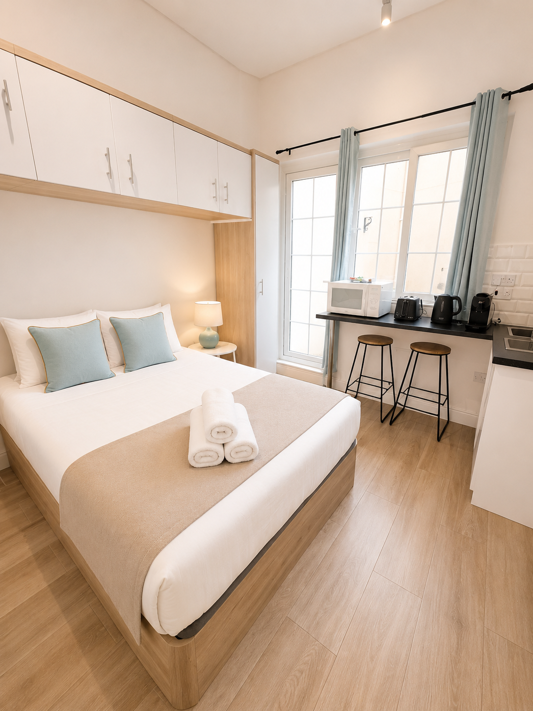 Bright minimalist bedroom with a bed, desk by a window, and pale wood flooring