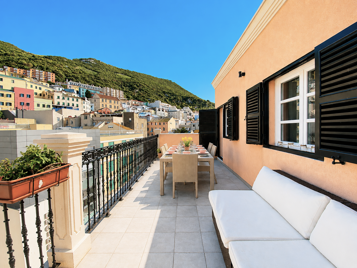 Balcony terrace with white sofa and table, overlooking colorful hillside buildings under a blue sky