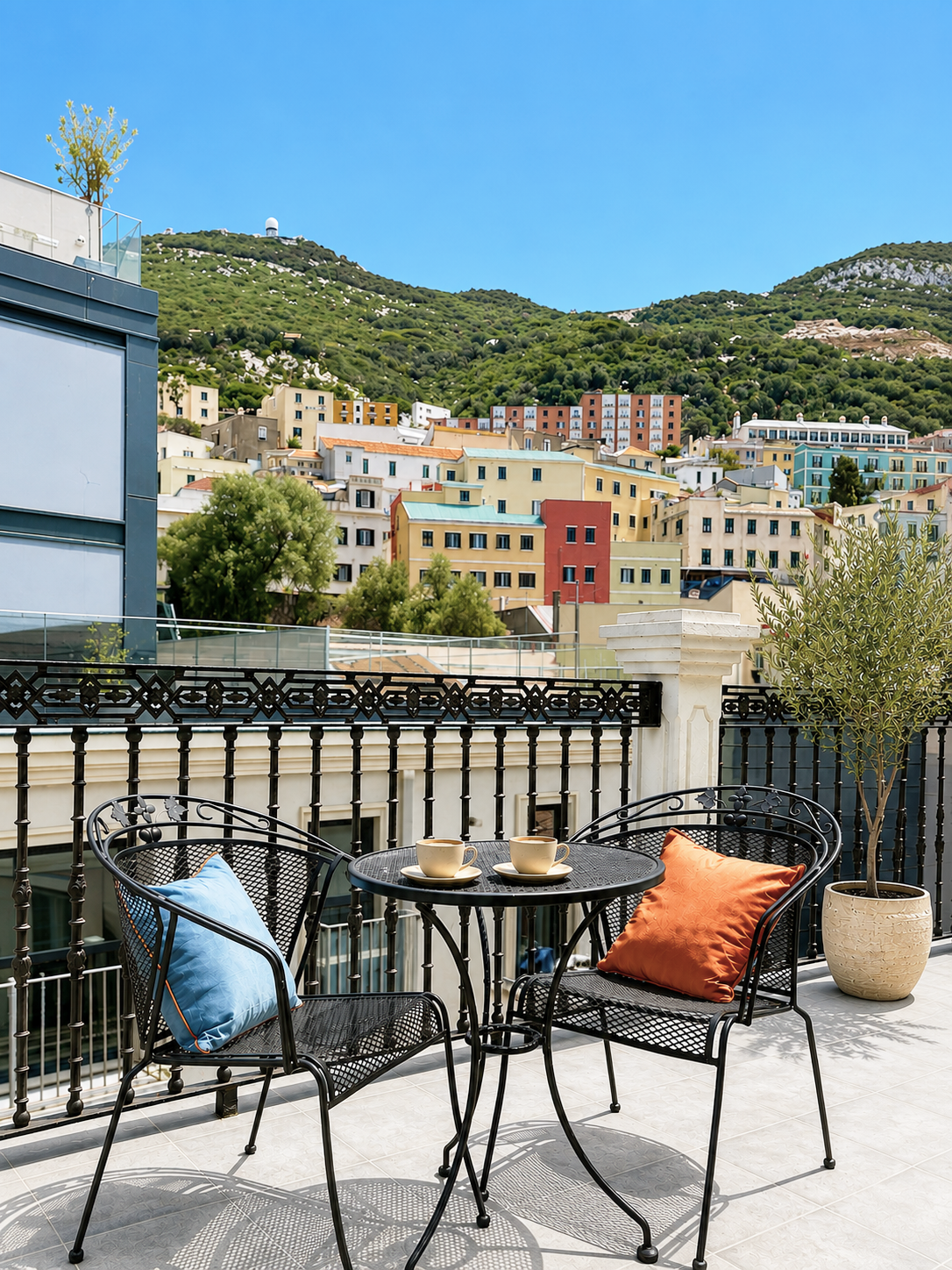 Balcony café seating with colorful chairs overlooking a hillside town and mountains