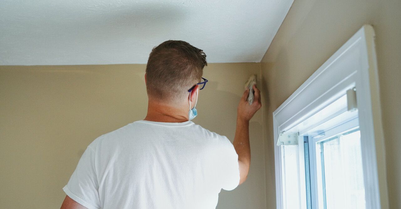 A man is painting a wall next to a window.