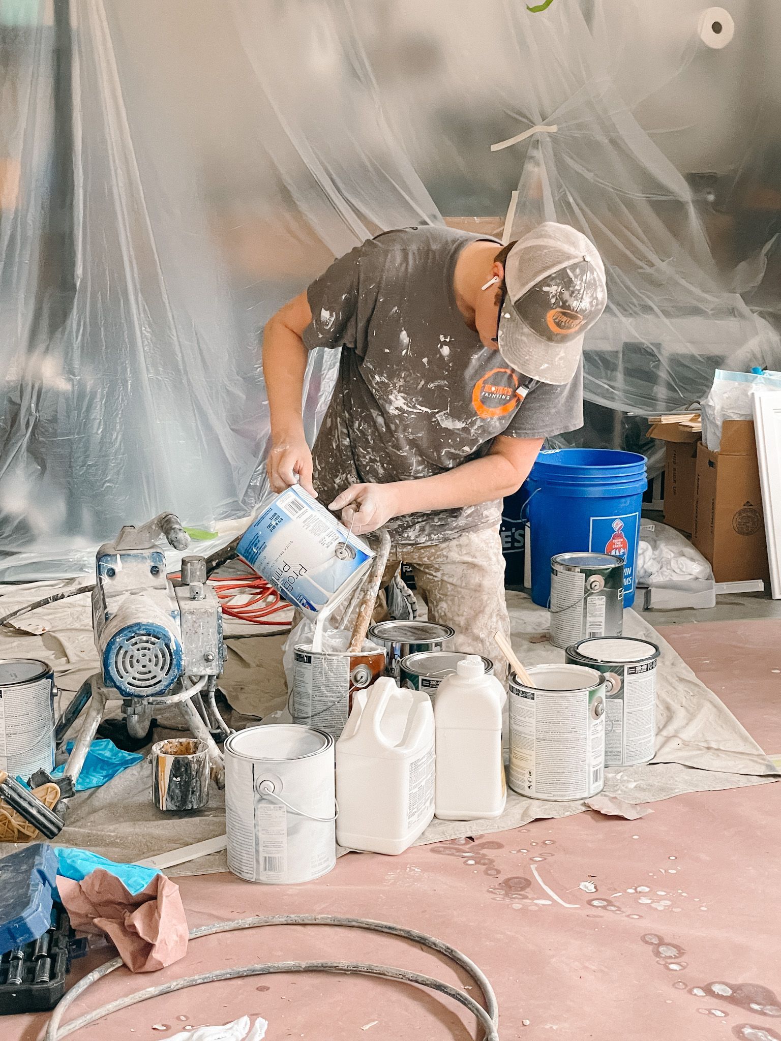 A man is pouring paint into a bucket in a room.