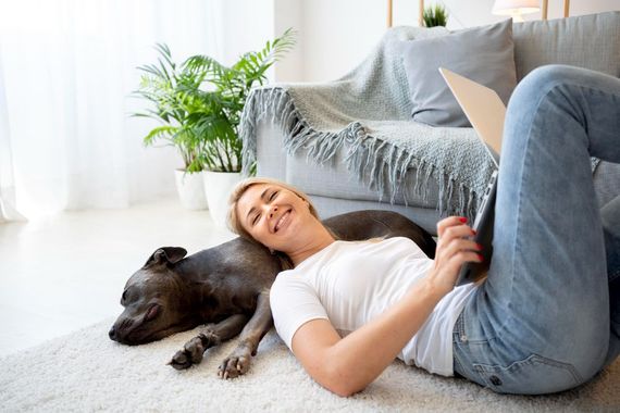 Woman lying on the floor with a dog beside a sofa in a bright living room
