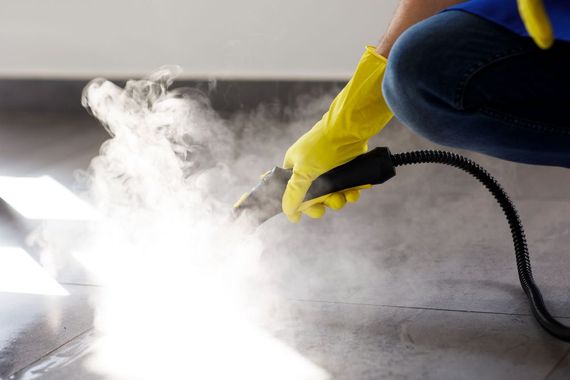 Person in yellow gloves using a steam cleaner on a floor, with thick white steam rising