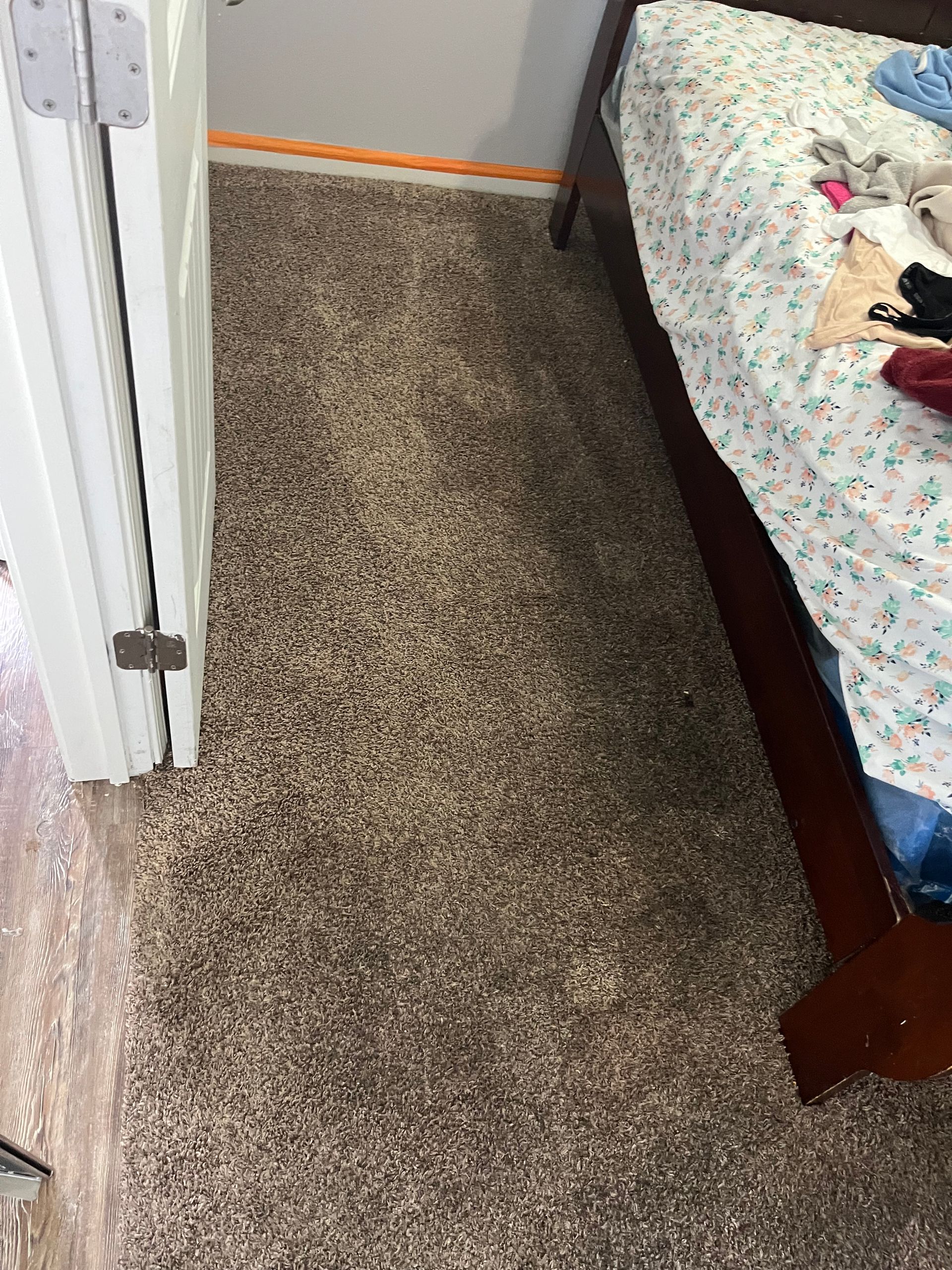 Narrow carpeted hallway beside an open bedroom door and bed with floral quilt