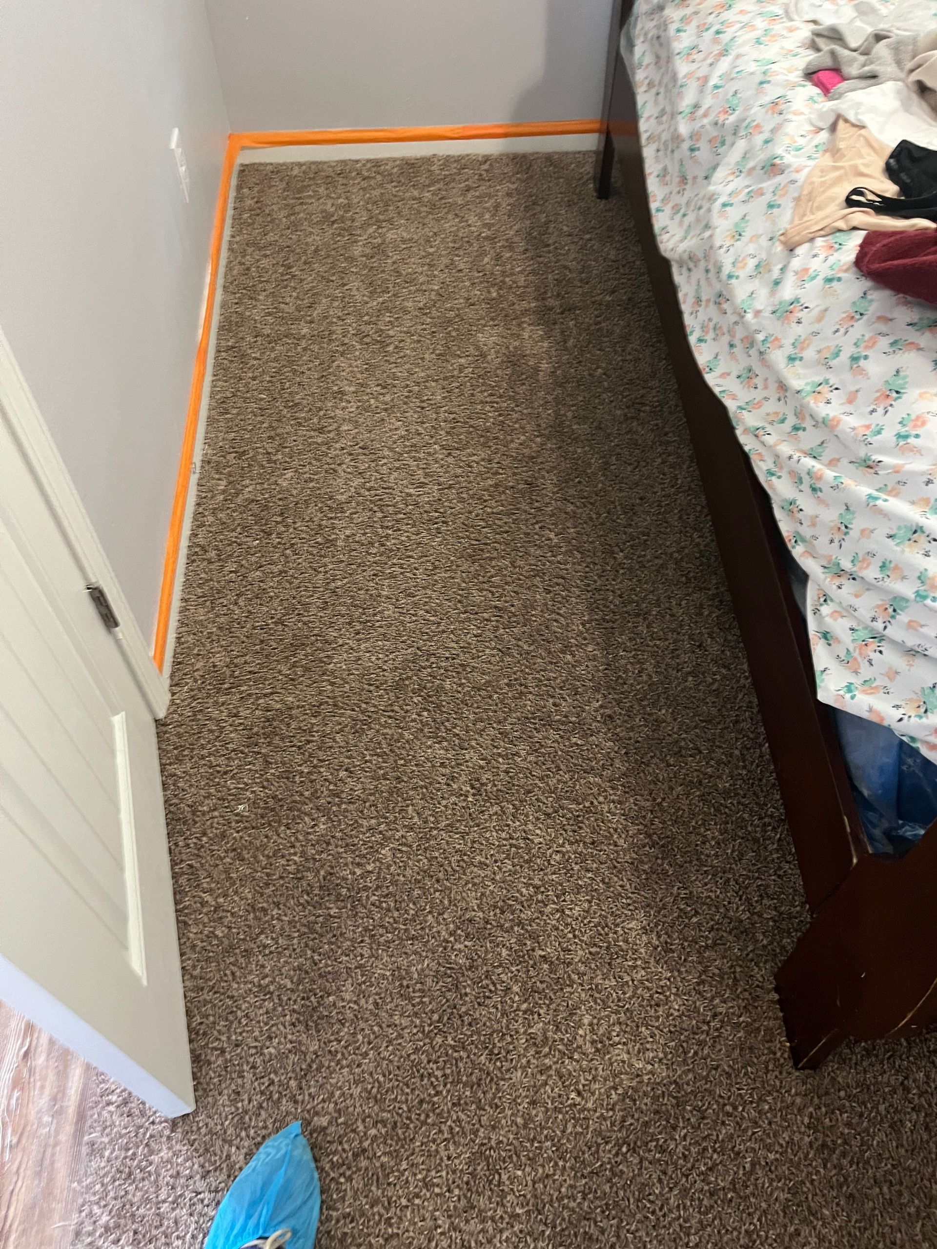 Narrow carpeted hallway beside a bed, with an open door and orange tape marking the floor edge.