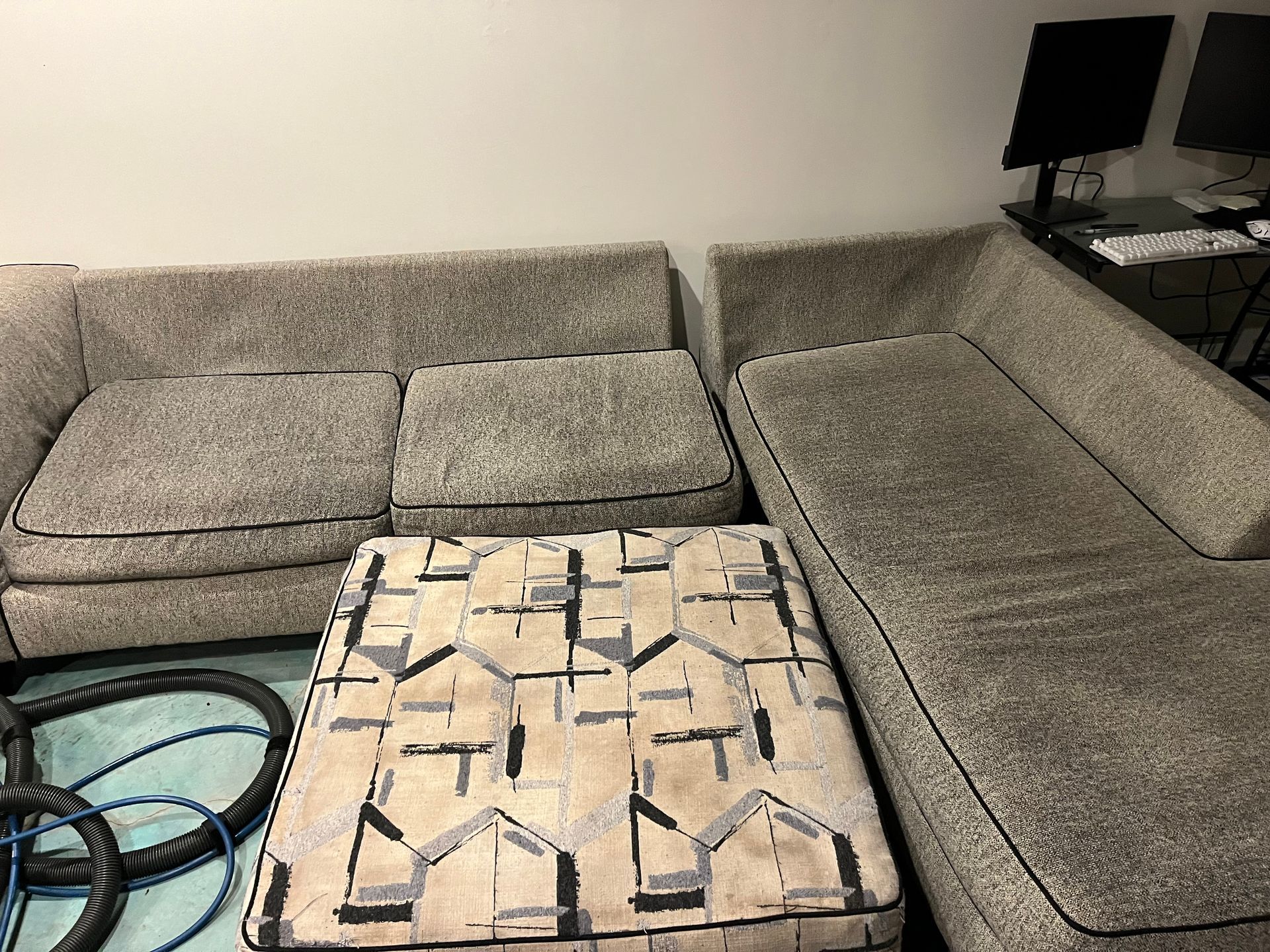 Gray sectional sofa around a small upholstered ottoman in a living room with a TV stand in the corner