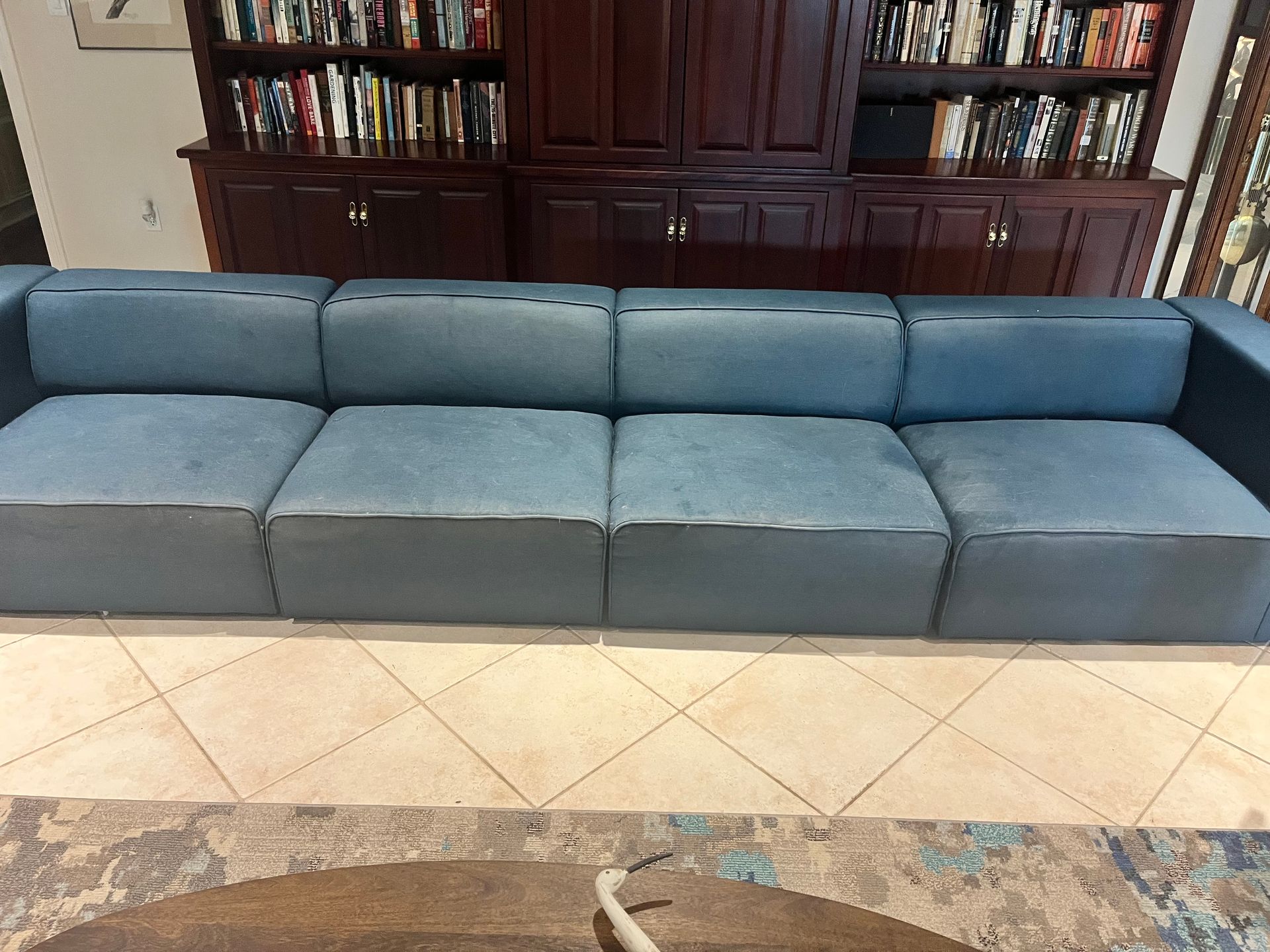 Blue sectional sofa in a living room with tiled floor and bookshelves in the background