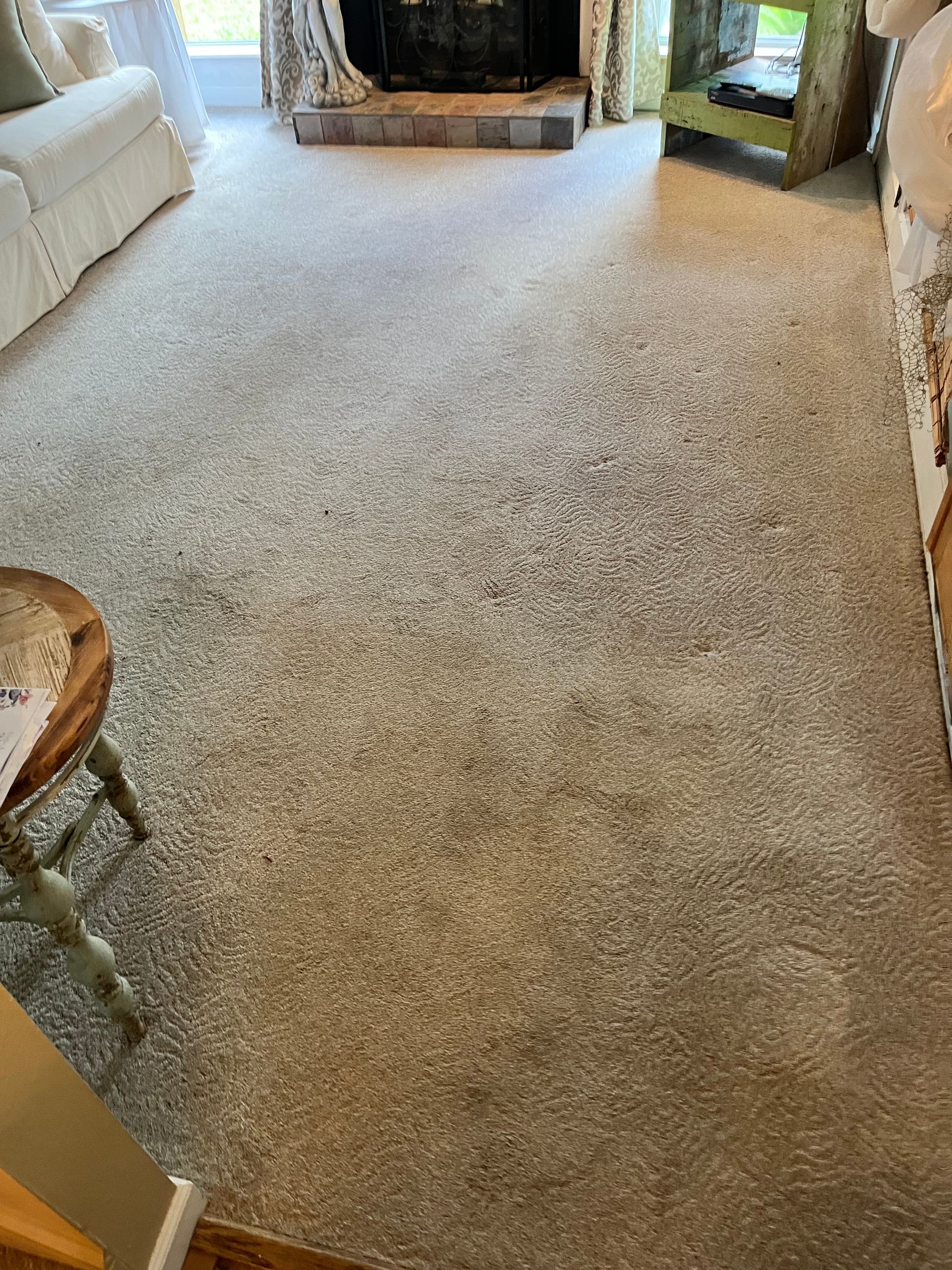 Carpeted living room with fireplace, sofa, and chair in warm neutral tones.