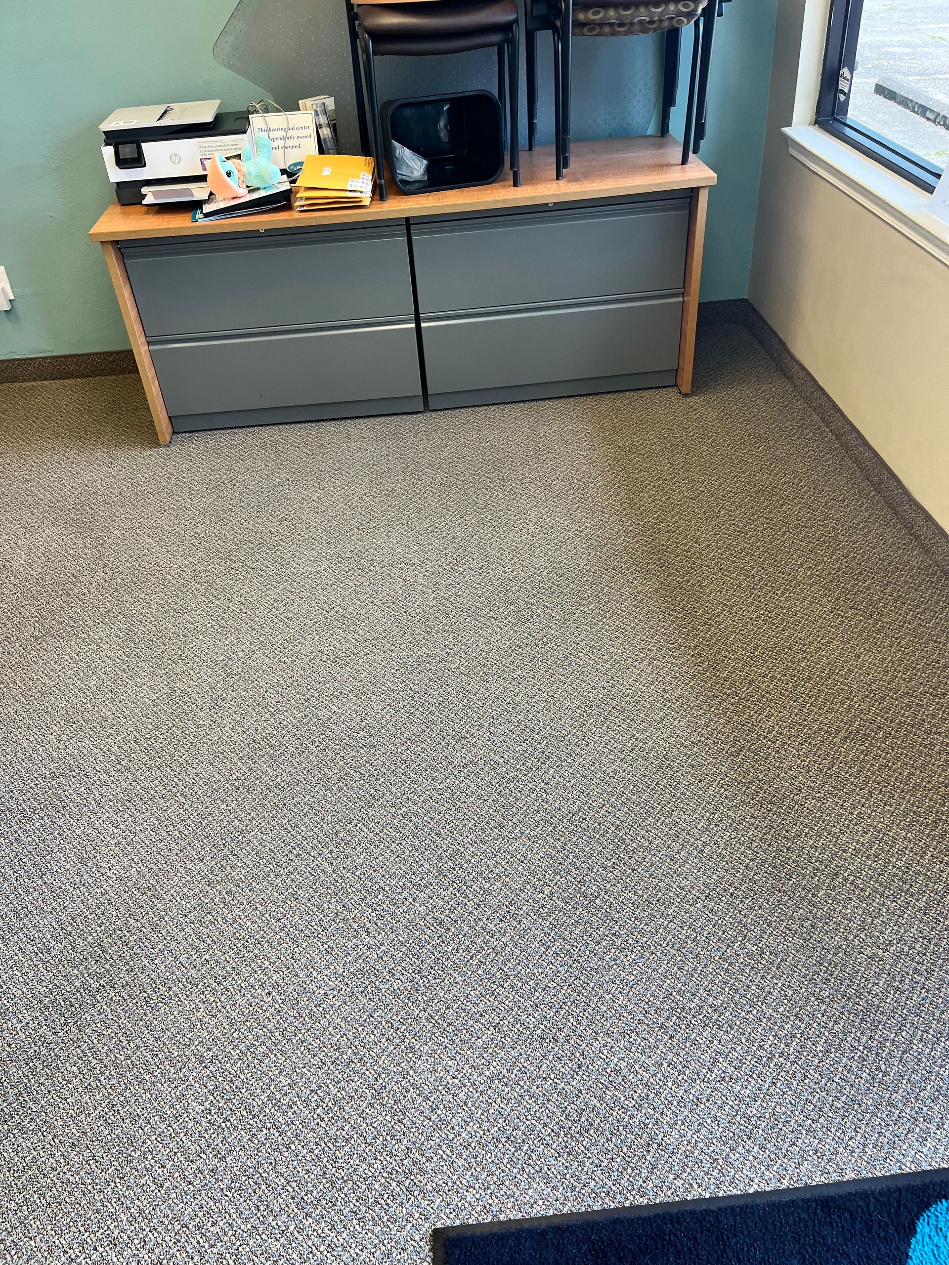 Office corner with gray carpet, low wooden cabinet, and window blinds.