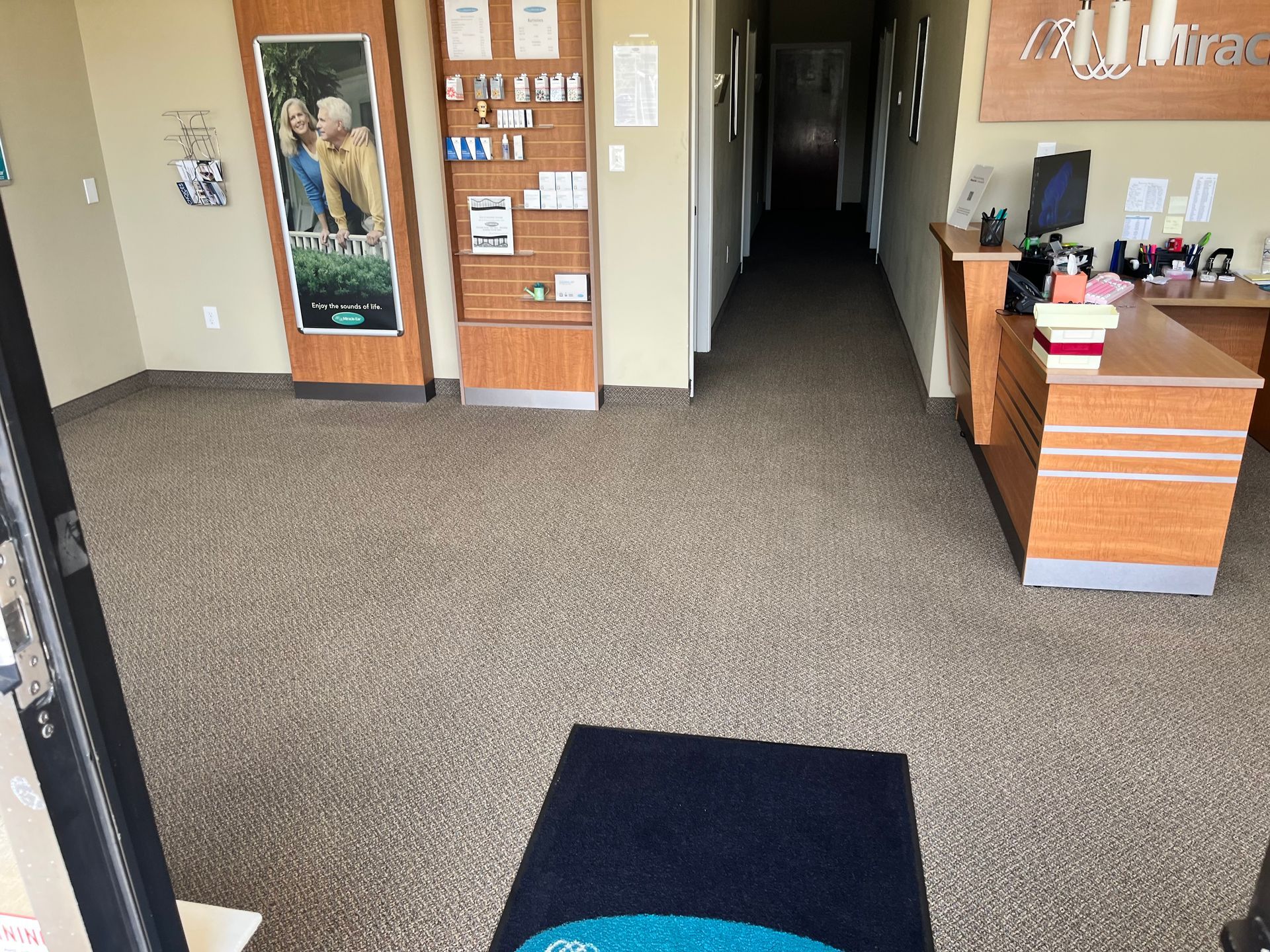 Office lobby with carpeted floor, reception desk, and hallway leading to a back corridor.