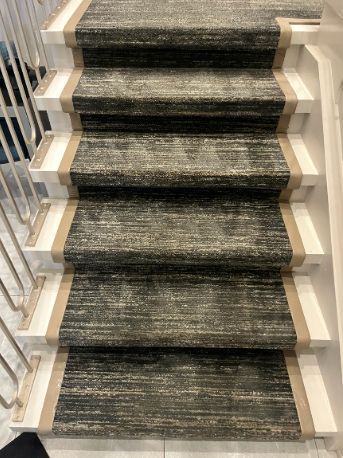 Carpeted indoor staircase with dark runner and light-colored side rails.