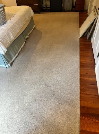 Bedroom with a beige rug beside a bed and hardwood floor.