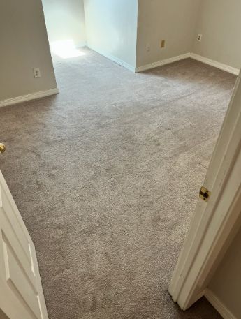 Empty carpeted hallway with beige walls and open doorways leading to a bright room