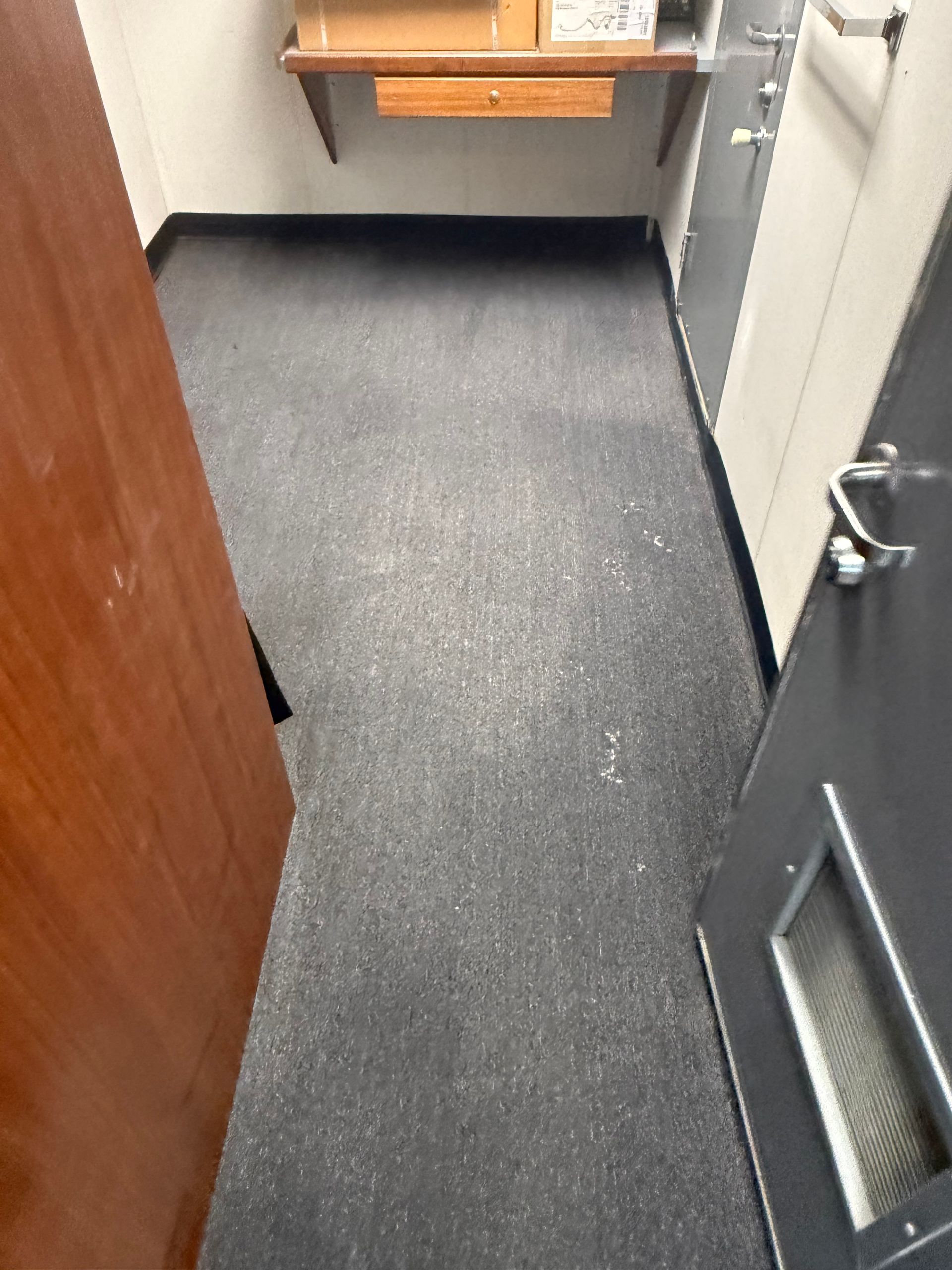 Narrow hallway with gray carpet, open doors, and a small desk at the far end.
