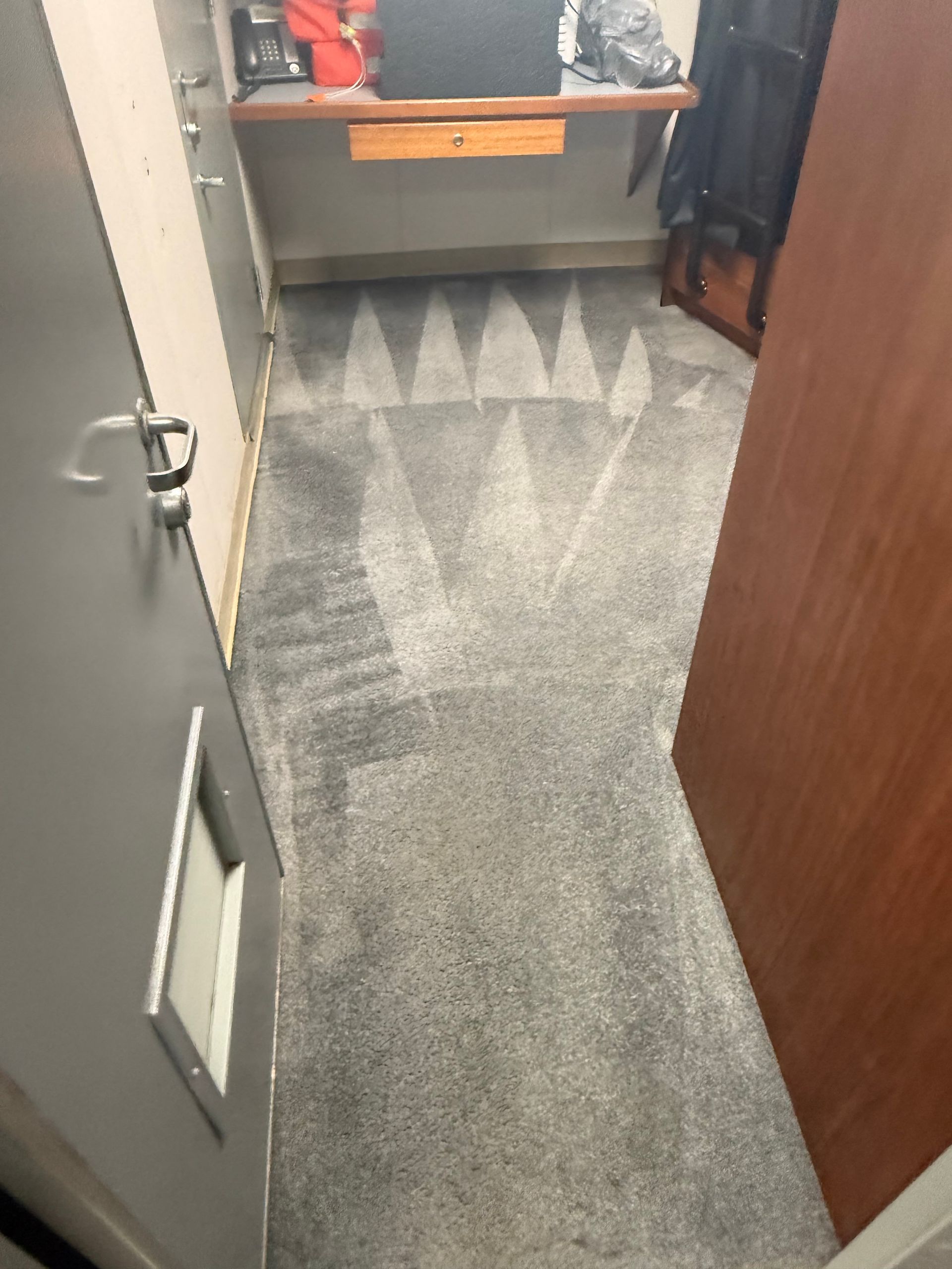 Narrow hallway with dark carpet, wooden cabinet, and open door with vent panel.