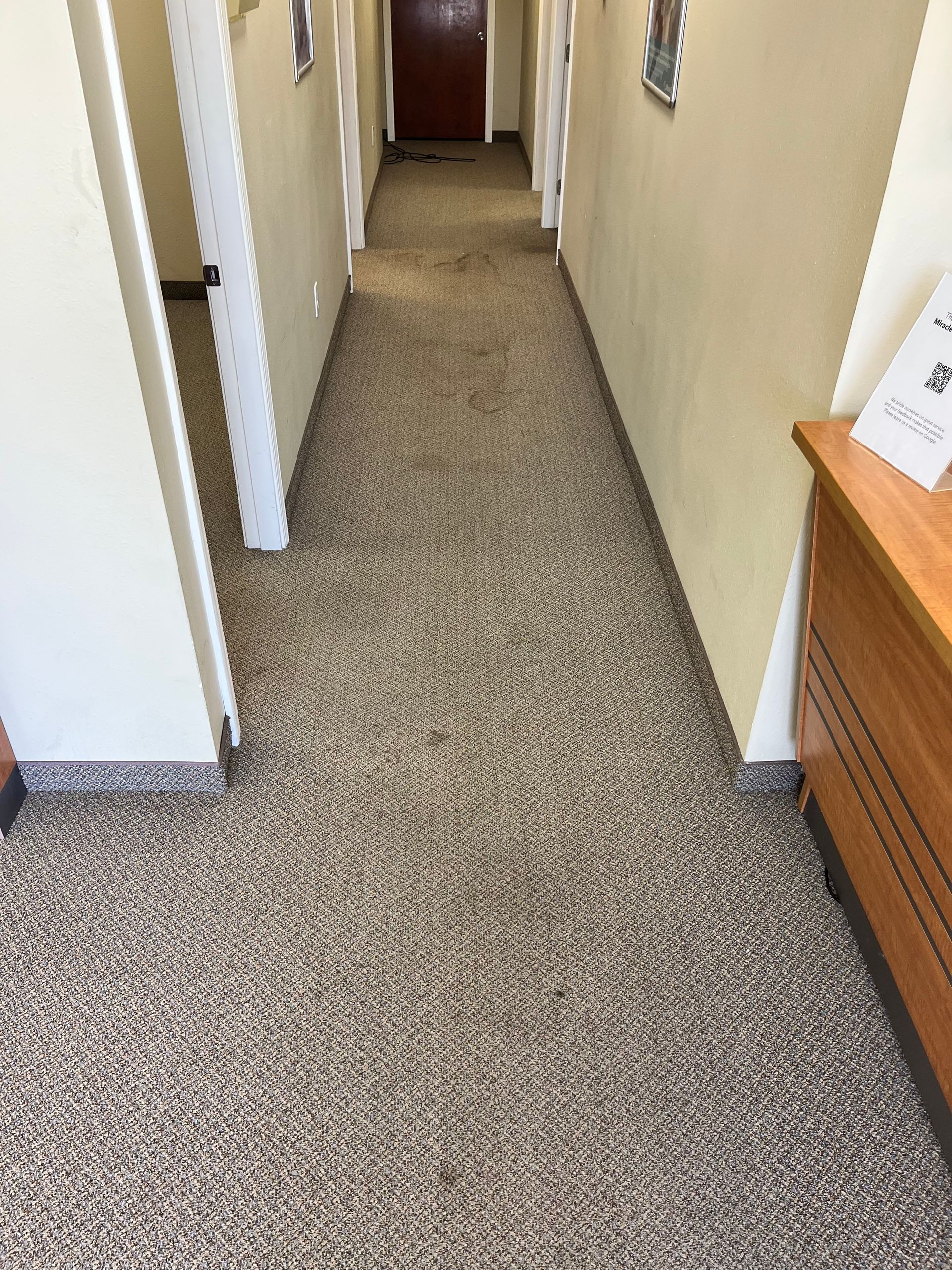 Narrow carpeted hallway with beige walls, white trim, and a wooden cabinet at the right