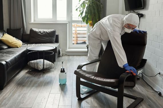 Person in protective gear disinfecting a black chair in a modern living room.