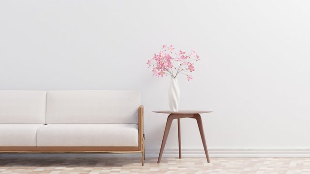 Minimal living room with a beige sofa, wooden side table, and vase of pink flowers against a white wall