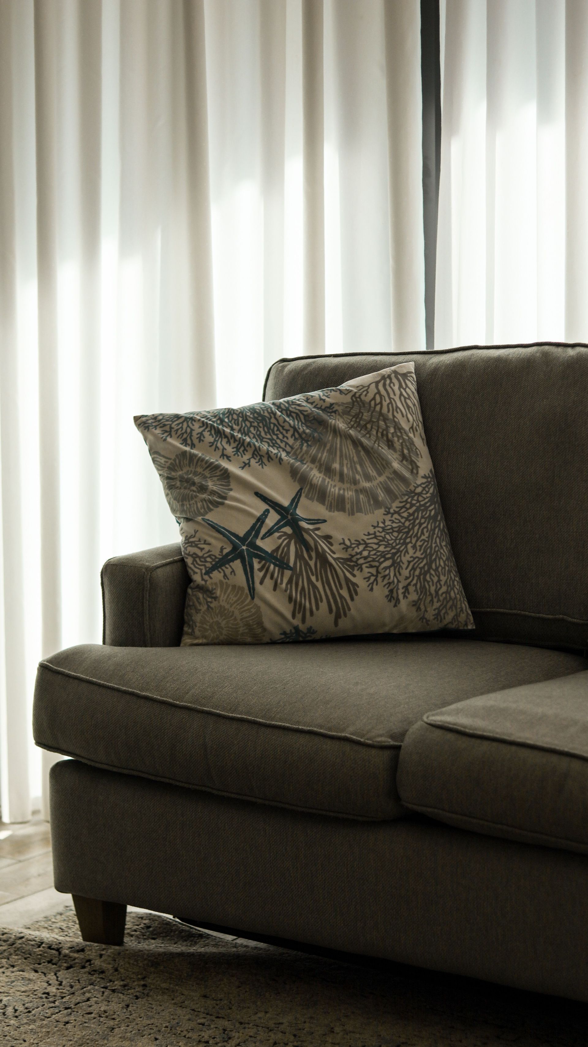 Dark gray sofa by sheer curtains with a patterned throw pillow