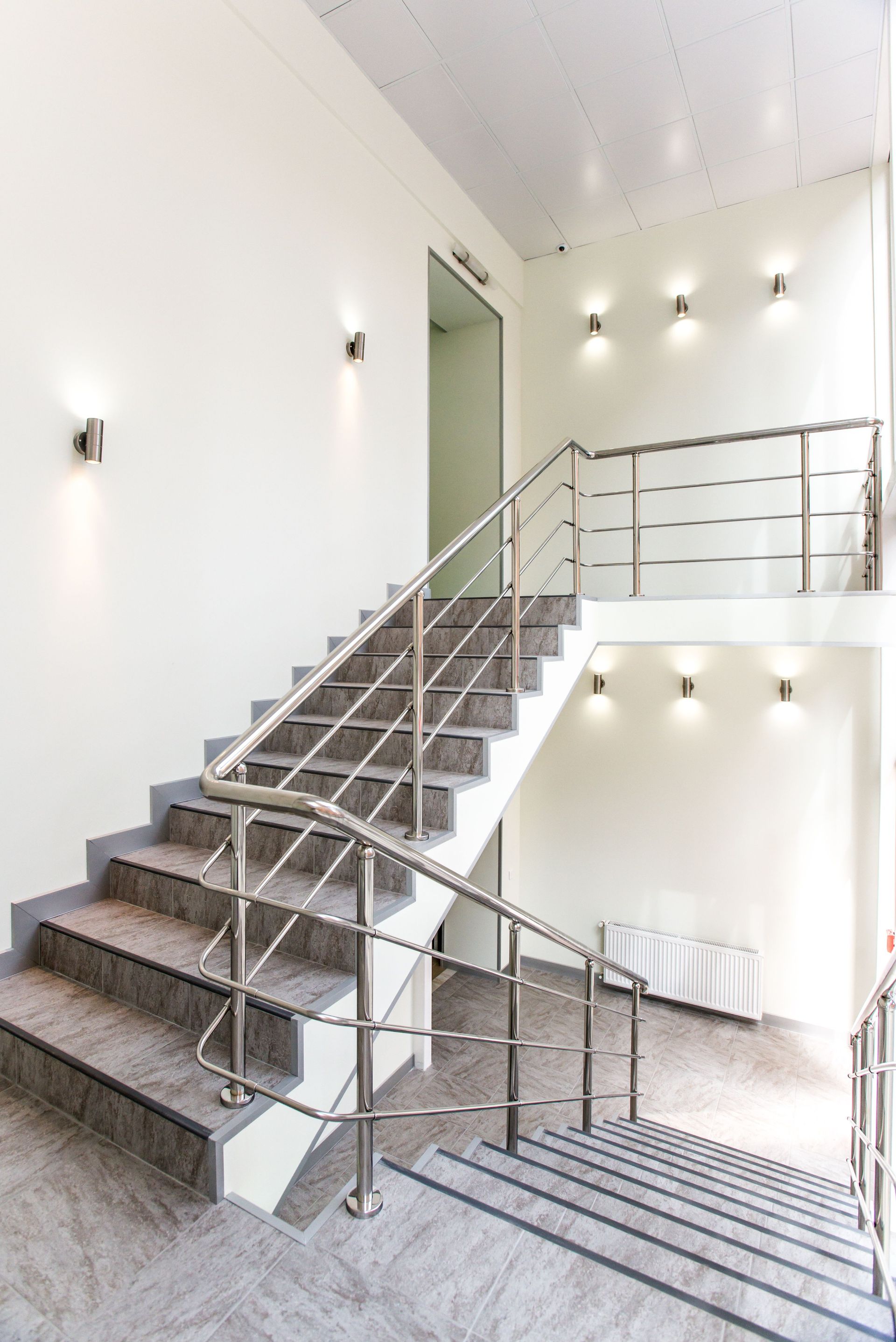 Modern indoor staircase with metal railings, white walls, and wall-mounted lights.