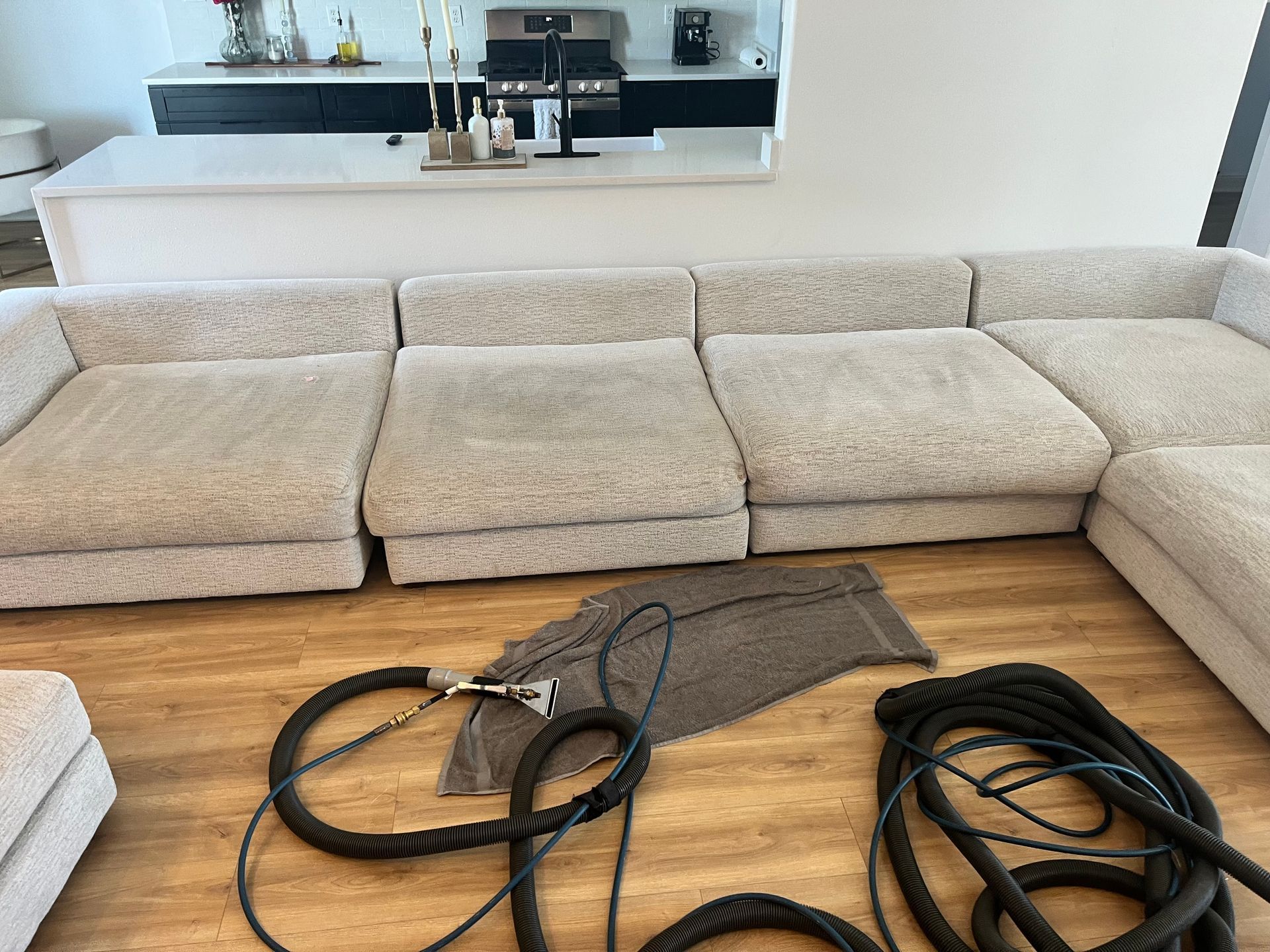 Sectional sofa in a living room with vacuum hoses and attachments laid out on the floor.