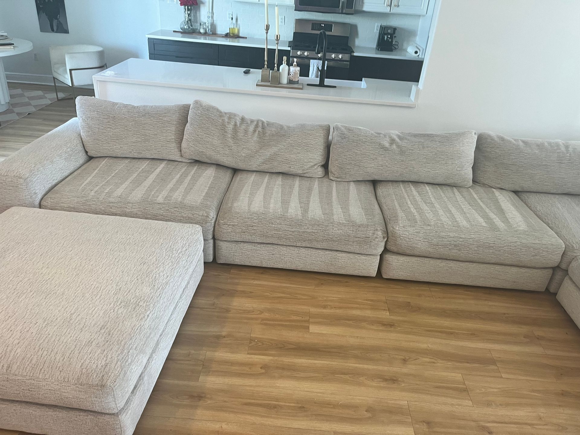 Beige sectional sofa in a bright living room with wood flooring and a kitchen in the background