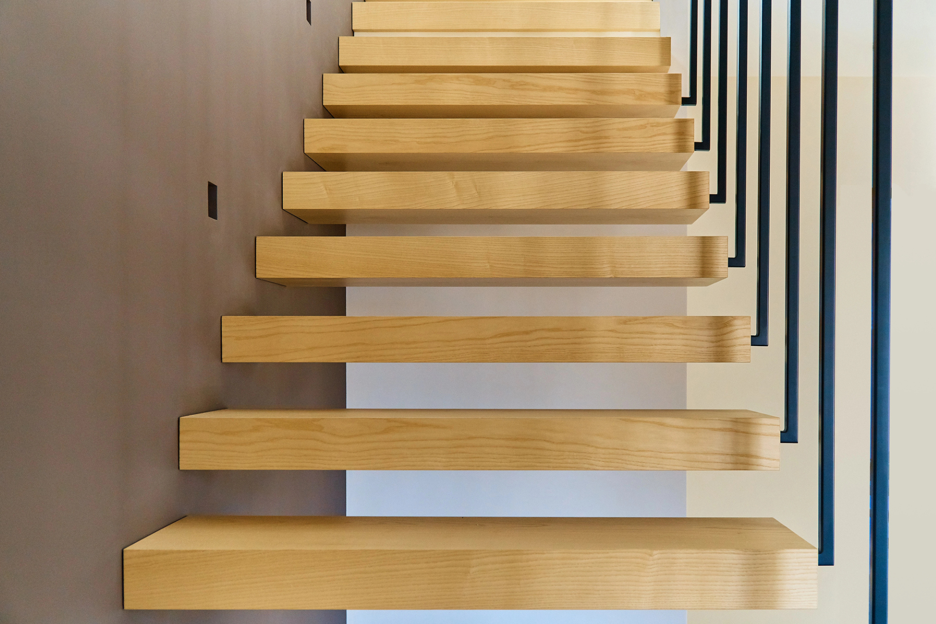 Modern wooden staircase with steps against a beige wall, complemented by sleek black railing.