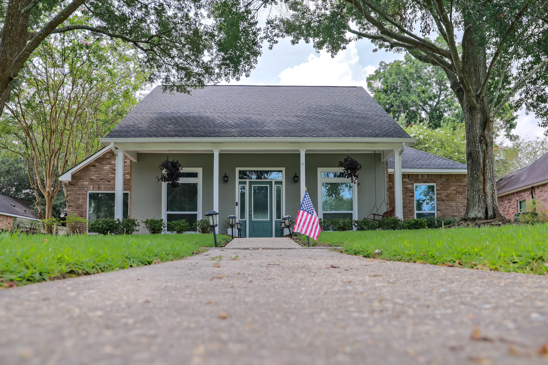An Acadian house with a large porch, framed by trees and green lawn. A small American flag