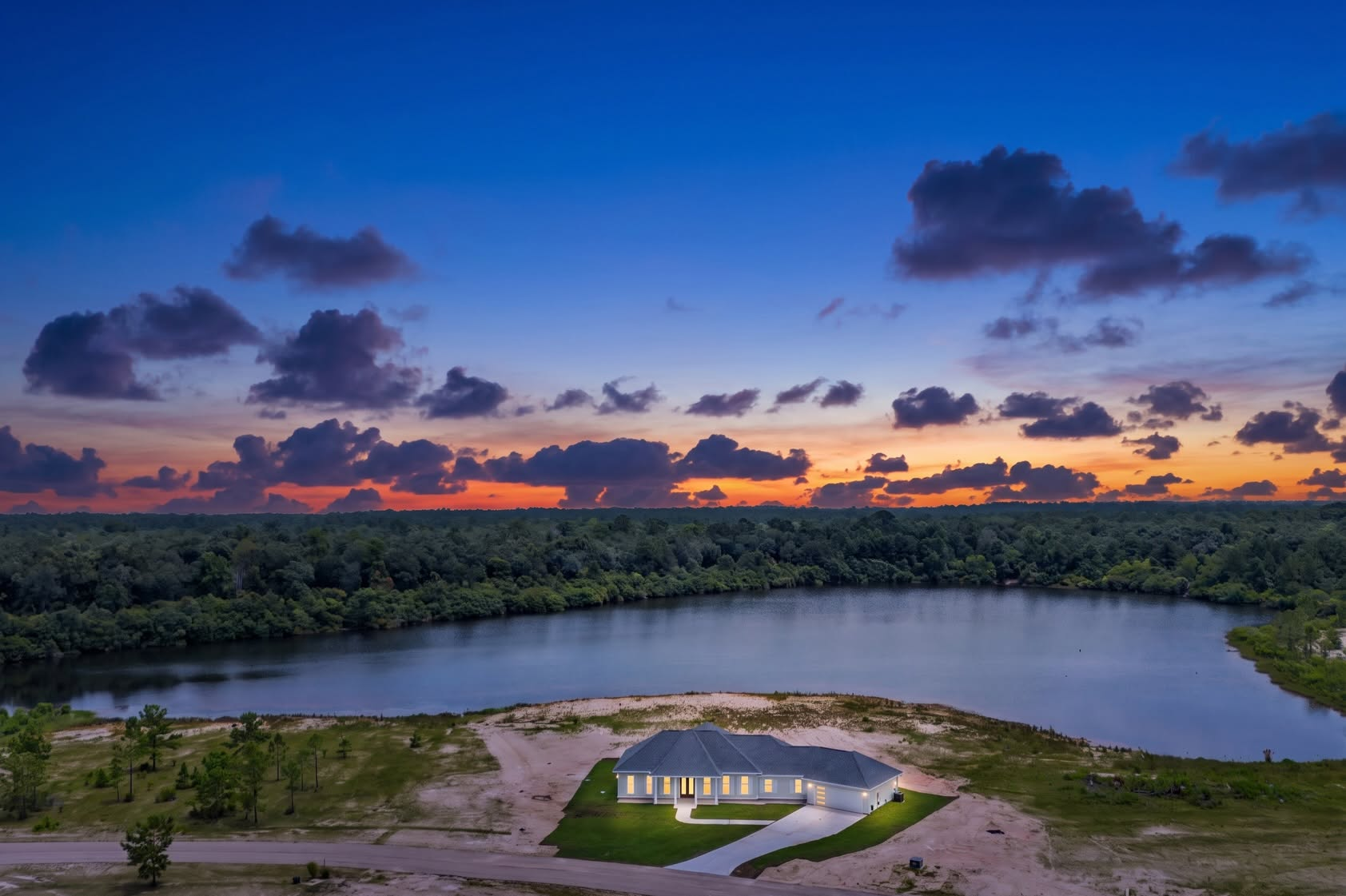 Aerial sunset view of an illuminated custom home beside a lake