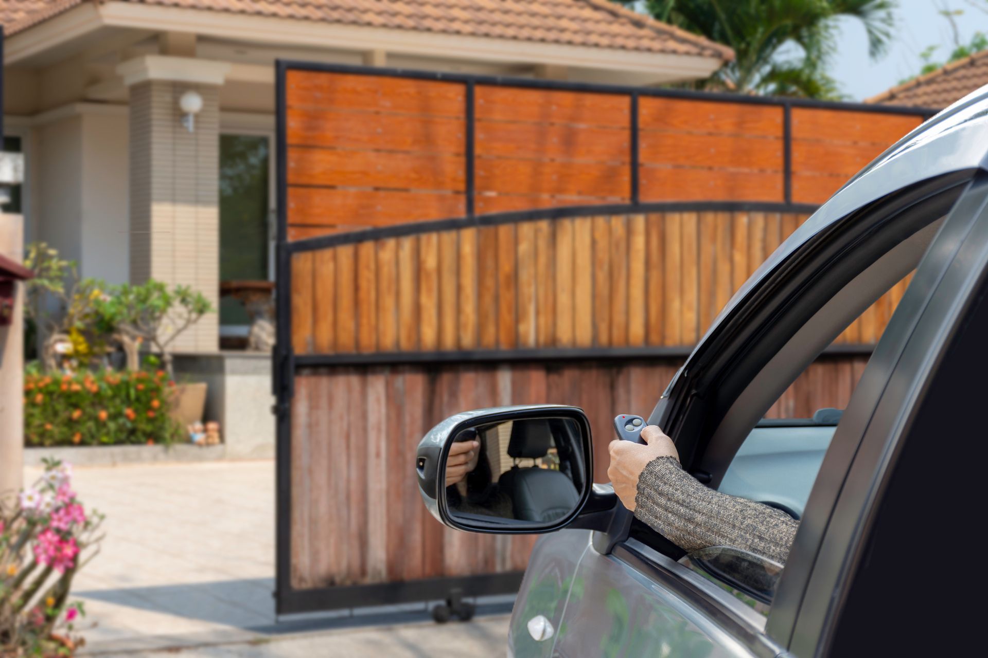 Person in car using remote to open a wooden gate to enter a house.