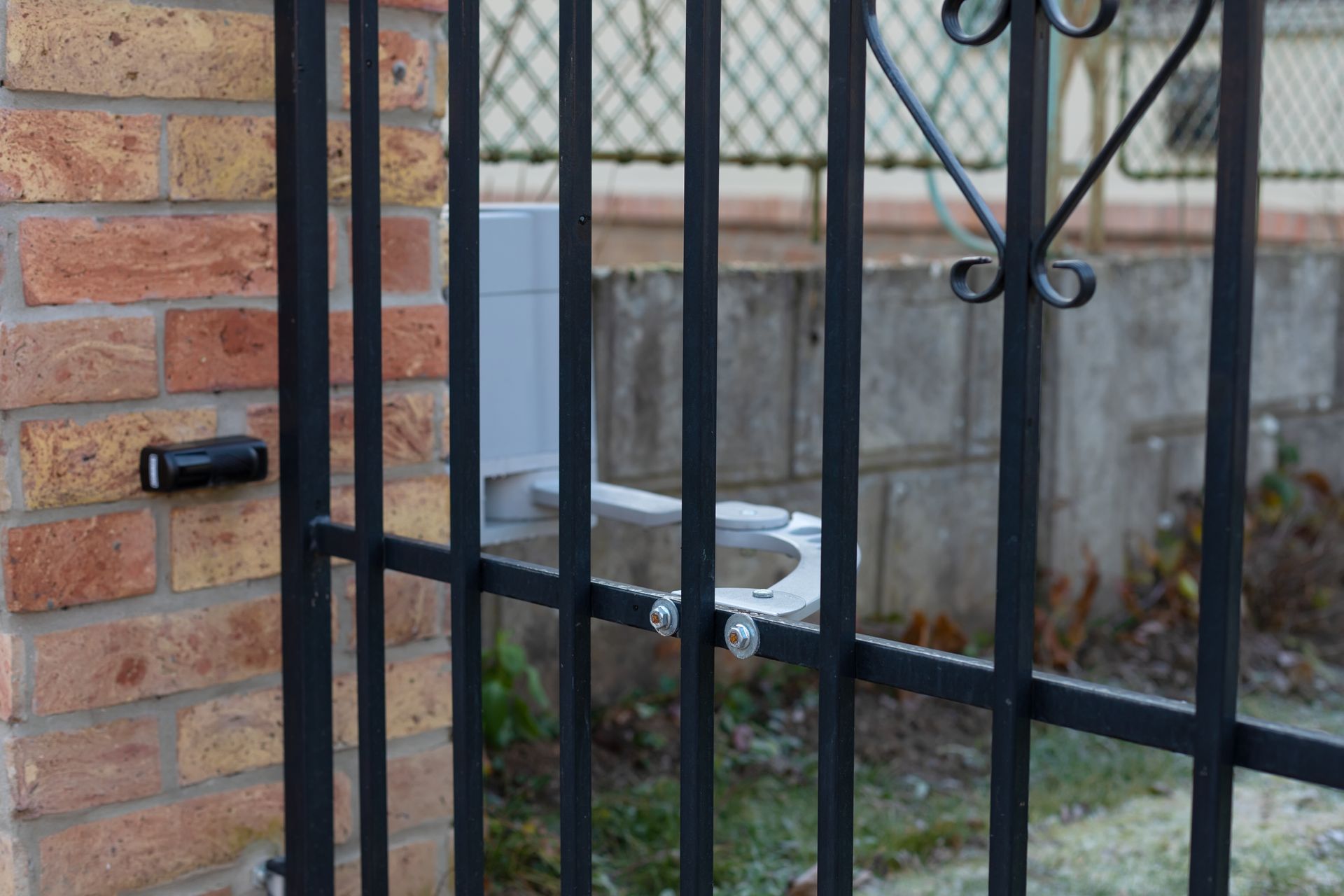 Black metal gate with automation mechanism on a brick pillar.