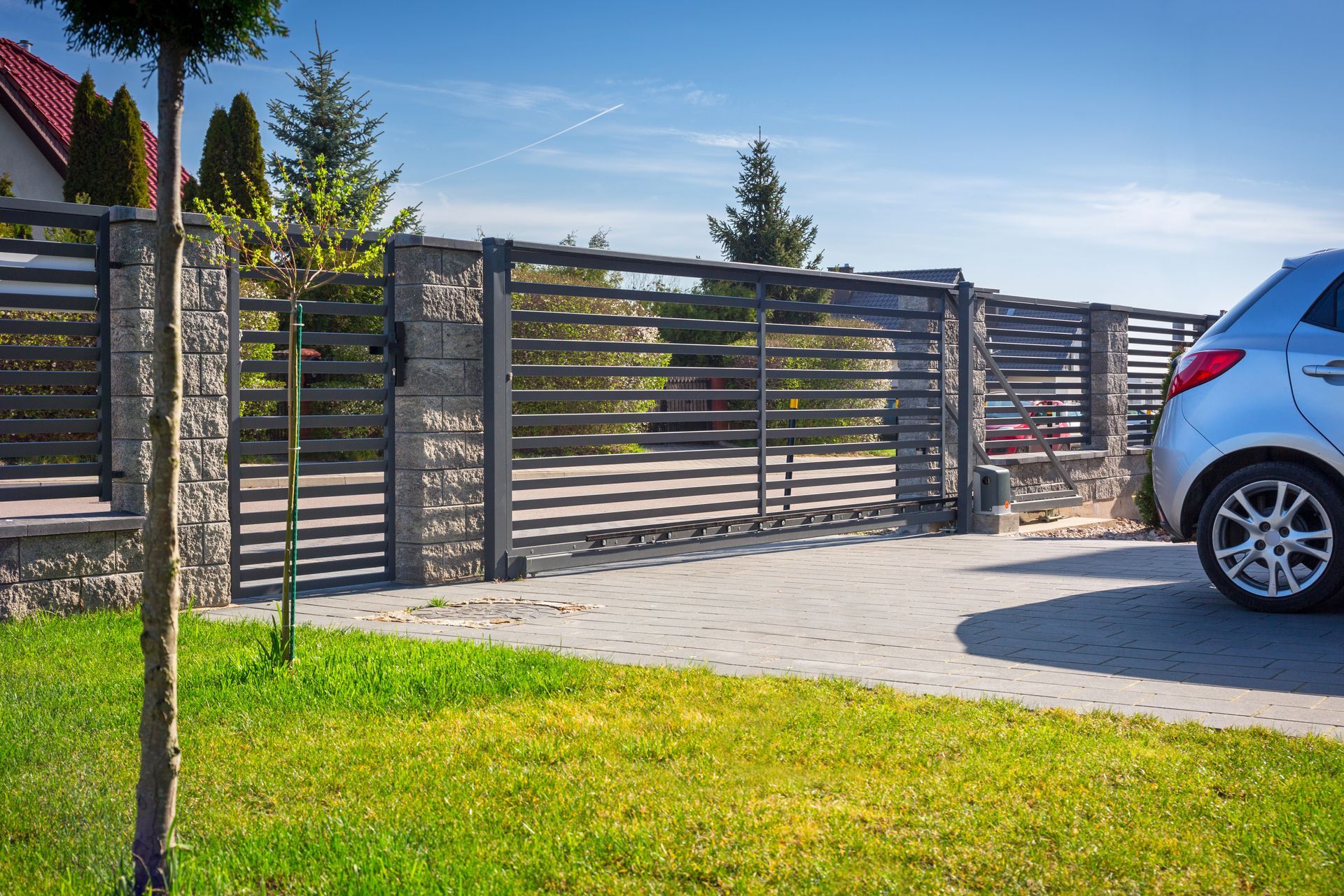 Grey horizontal slat driveway gate and fence with a silver car parked on a paved driveway.