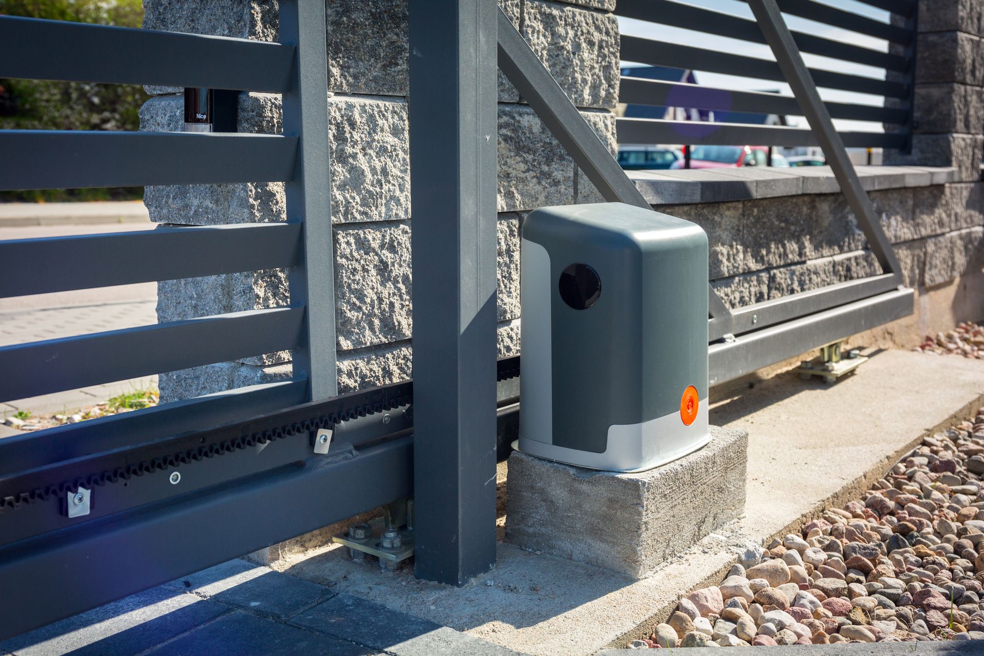 Gray automatic sliding gate with motor, installed on a concrete base, next to a stone pillar.