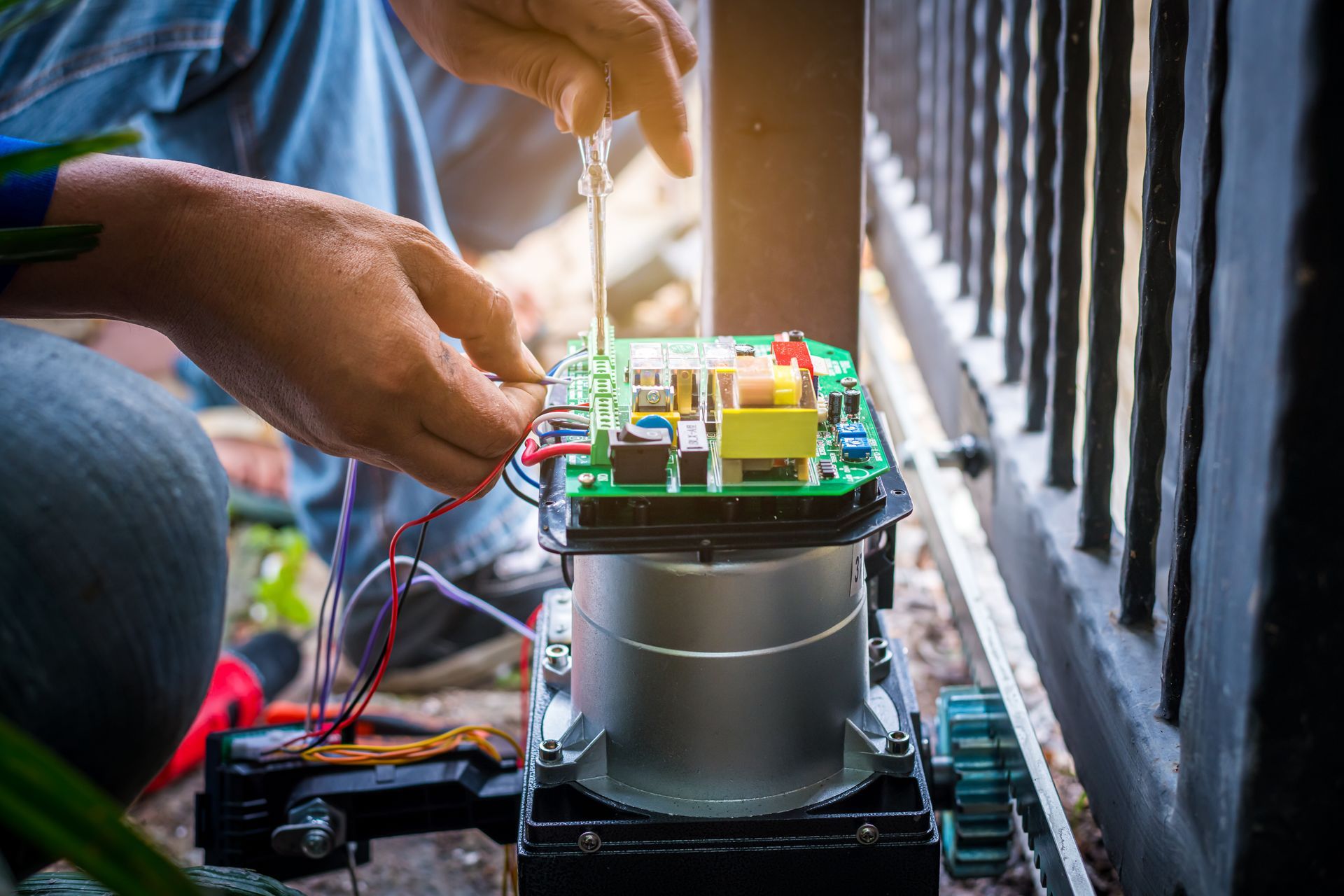 Person wiring an automatic gate opener, outdoors.