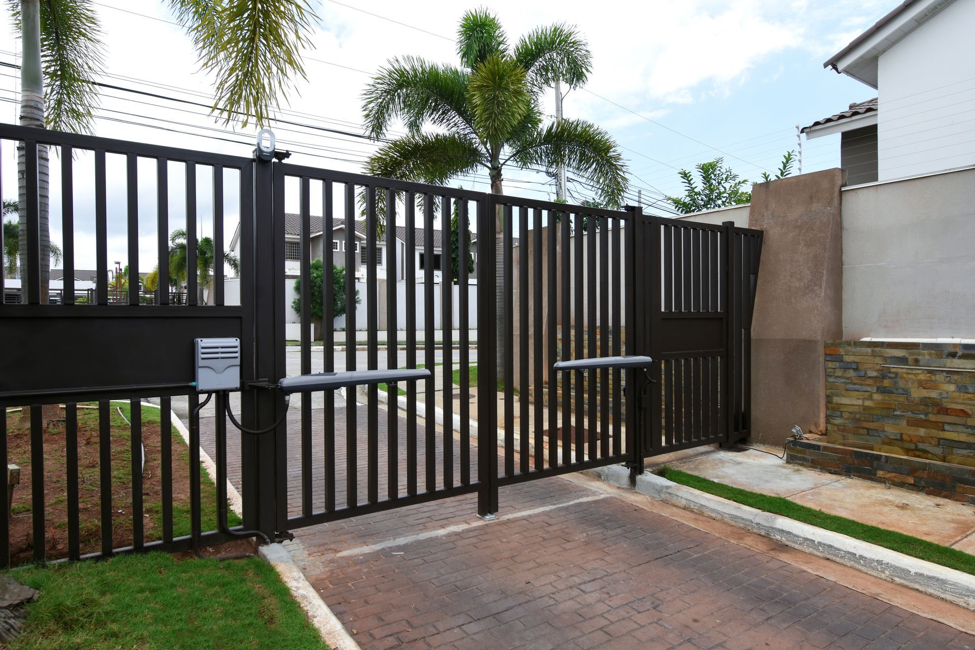 Dark metal gate, open, with an automatic opener. Driveway and residential yard in view.