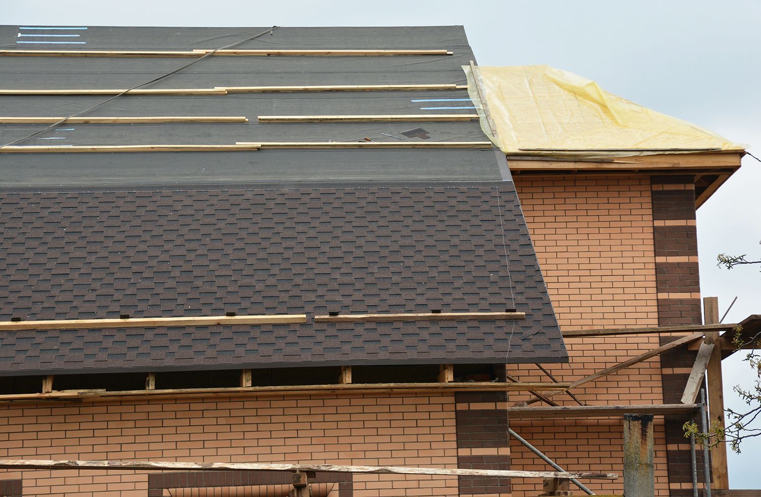 Roof under construction on a brick building, with dark shingles and exposed yellow underlayment.