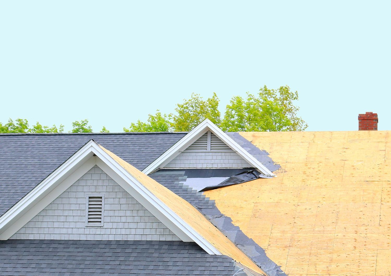 Roofing work on a gray house, with a partially covered roof and blue sky above.