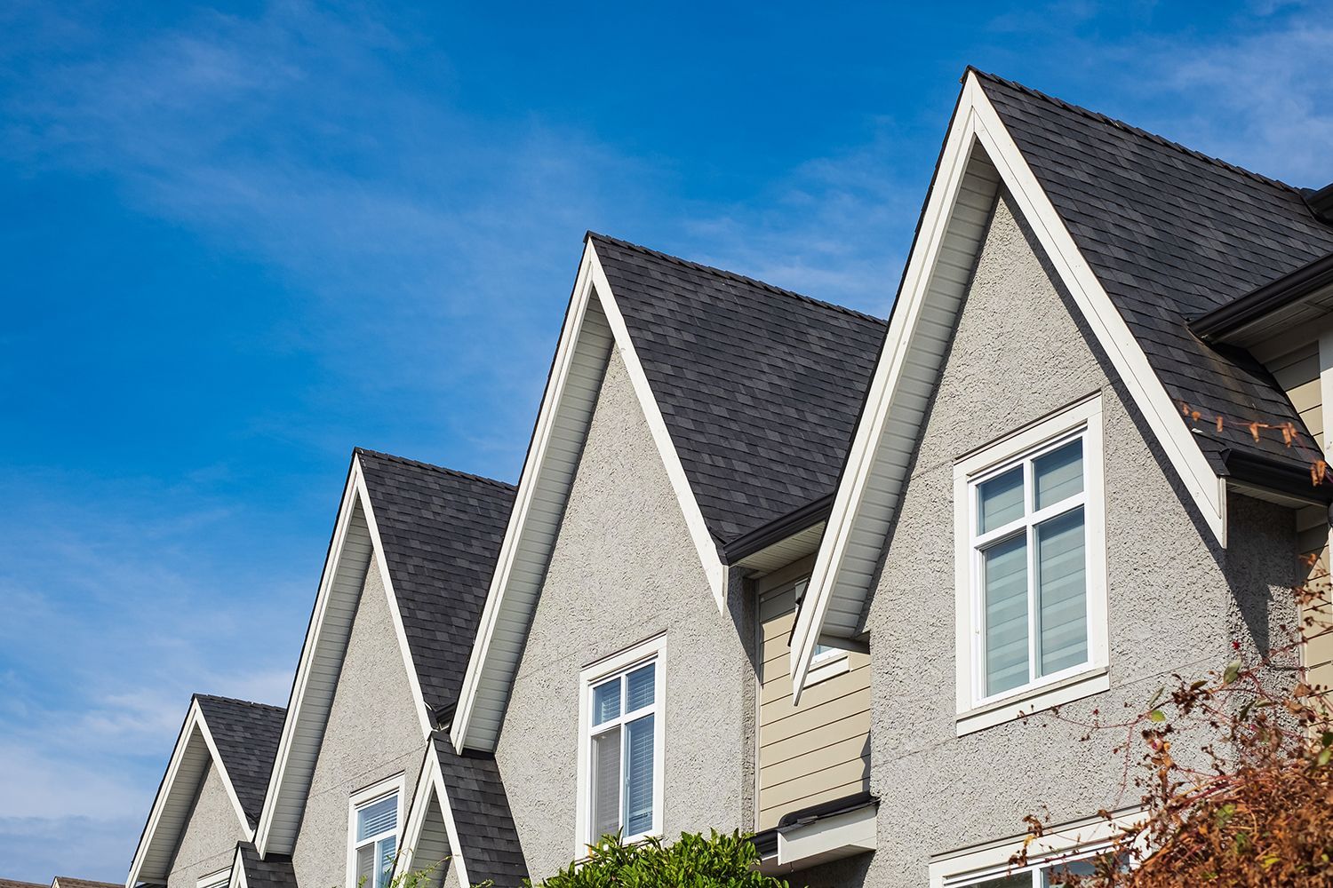 Row of gray townhouses with steep gabled roofs under a blue sky