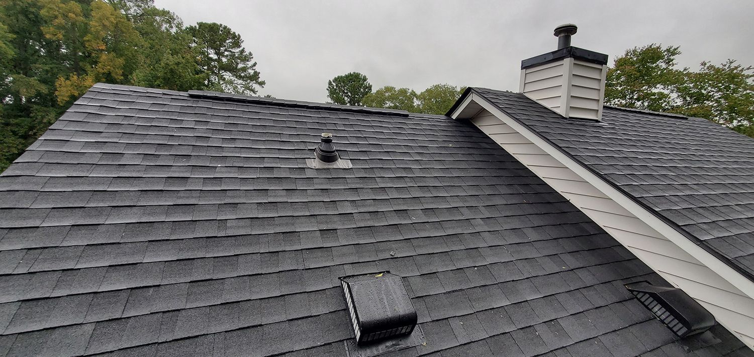 Gray shingled roof with two vents and a chimney under cloudy skies