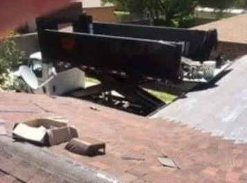 Damaged black truck cab sticking through a roof opening with broken shingles around it