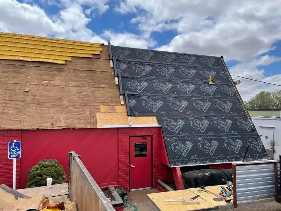 Damaged storefront with exposed roof, red wall, and black tarp covering part of the building.