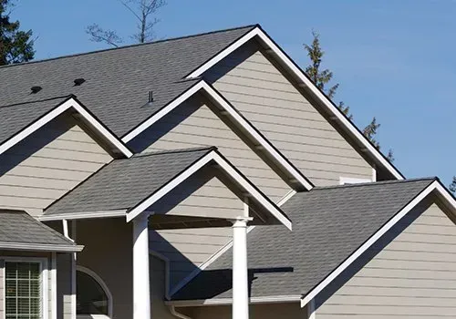 Suburban house rooflines with gray shingles and beige siding under a blue sky