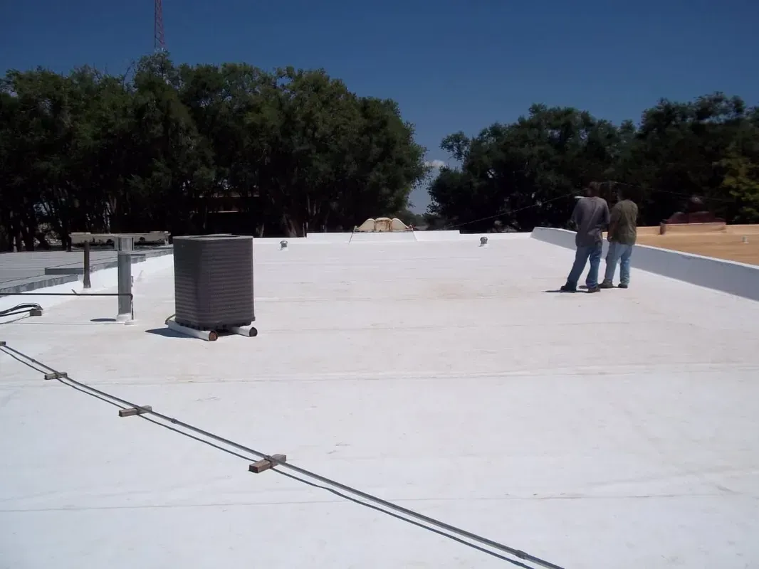 Flat white rooftop with two workers standing near an HVAC unit under a clear blue sky.